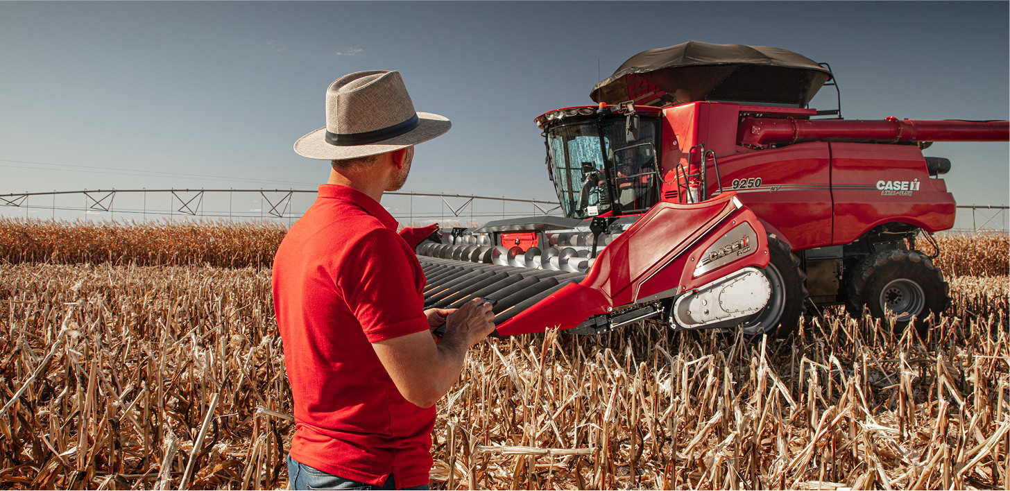 Homem de costas com uniforme da Case IH no campo olhando para uma colheitadeira Axial-Flow 9250 e segurando um celular nas mãos.