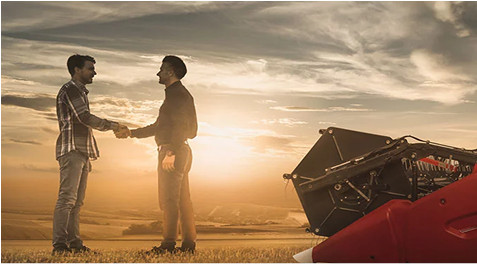 Agricultor e consultor homologado da Case IH apertando as mãos em frente de uma plataforma Draper Case IH durante o pôr do Sol em uma fazenda